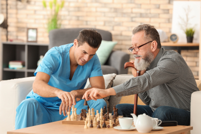 young caregiver and senior man playing chess at home